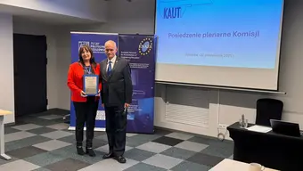 Uczestnicy posiedzenia, kobieta i męzczyzna stoją obok siebie, zwróceni do aparatu